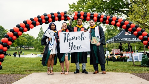 Four graduates standing in front of a 'Thank You' sign.