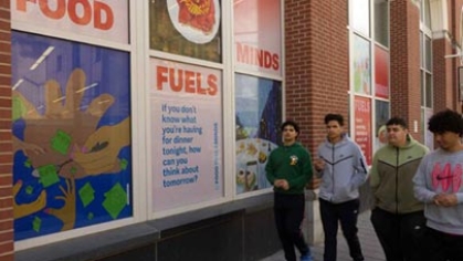 Four people walking past a sign that says, 'Food Fuels minds'.