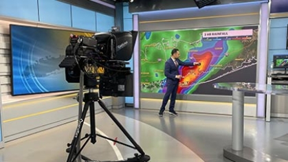 A meteorologist giving a televised weather forecast on a sound stage.