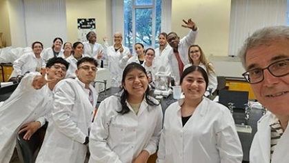 A professor and a group of students wearing lab coats in a lab.