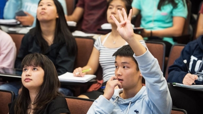 A student in a lecture hall raising their hand.