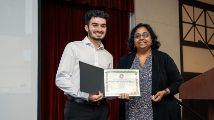 A student holding an award standing next to a faculty member.