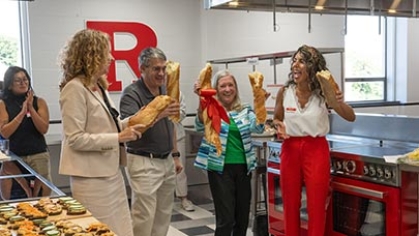 Four people holding up loaves of bread in a test kitchen.