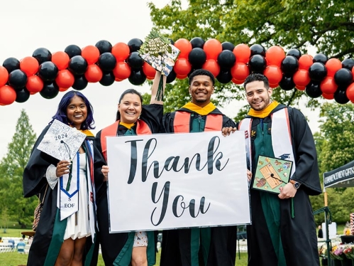 Four graduates standing in front of a 'Thank You' sign.